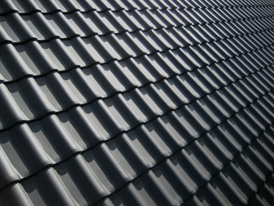 Toiture en tuiles gris anthracite : rangées régulières vues en enfilade, sous une lumière rasante.