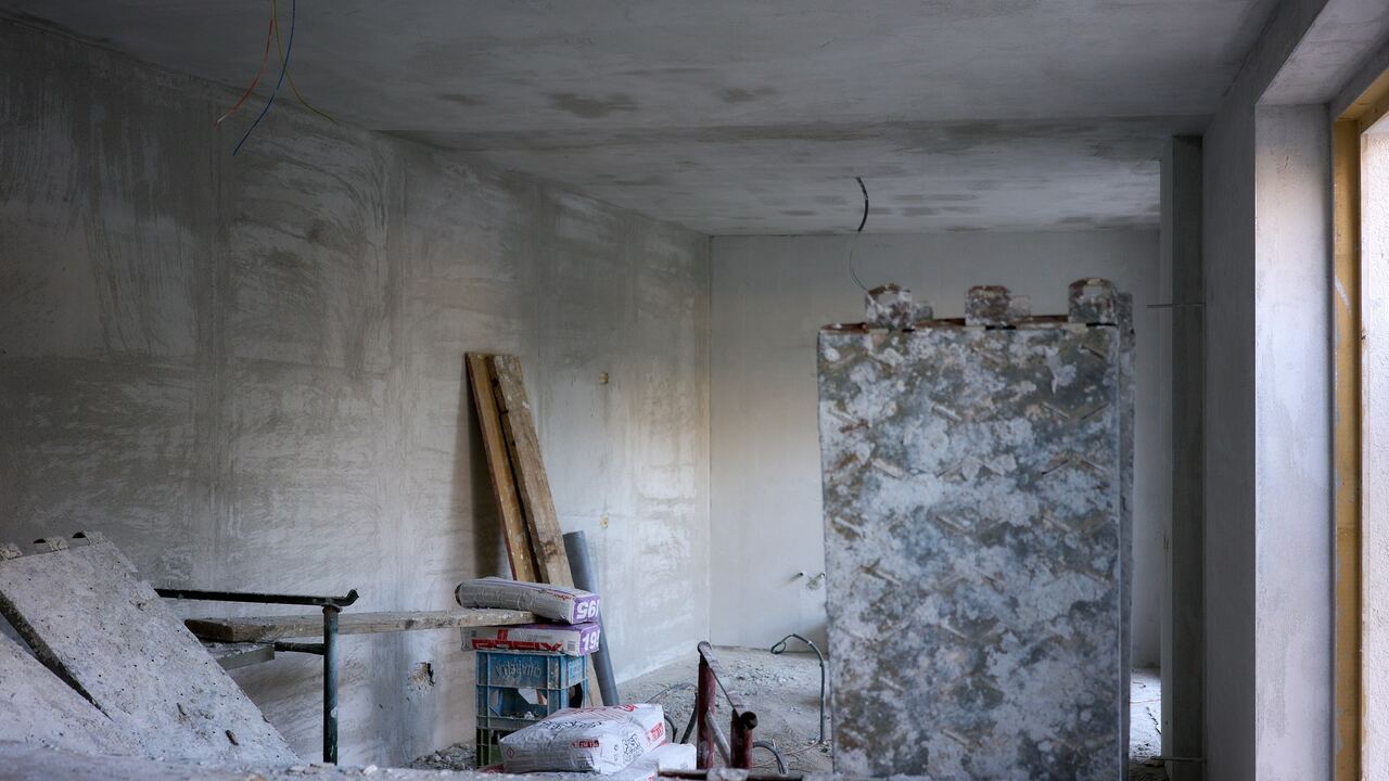 Pièce au stade du gros œuvre : murs et plafond en béton brut, panneau de coffrage métallique, planches et sacs de matériaux au sol.