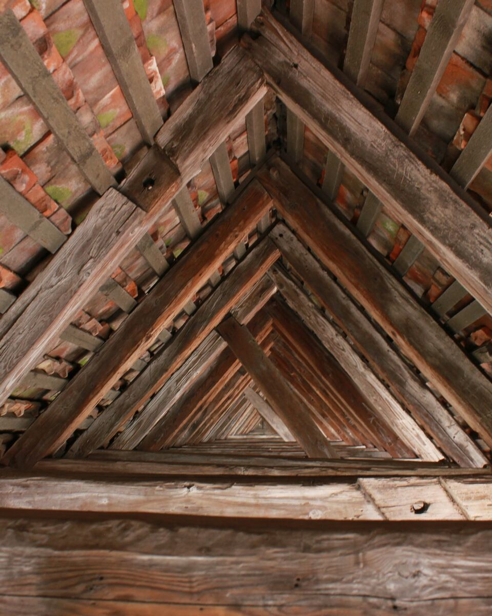 Charpente ancienne vue de l’intérieur : chevrons et pannes en bois forment une suite de triangles sous les tuiles.