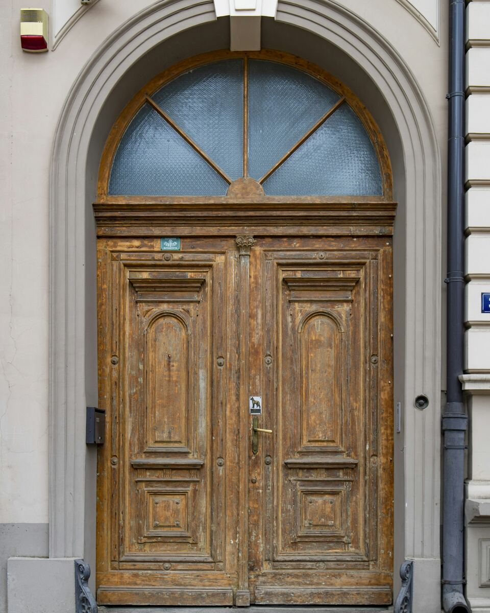 Porte d’entrée double en bois patiné, surmontée d’une imposte vitrée cintrée.