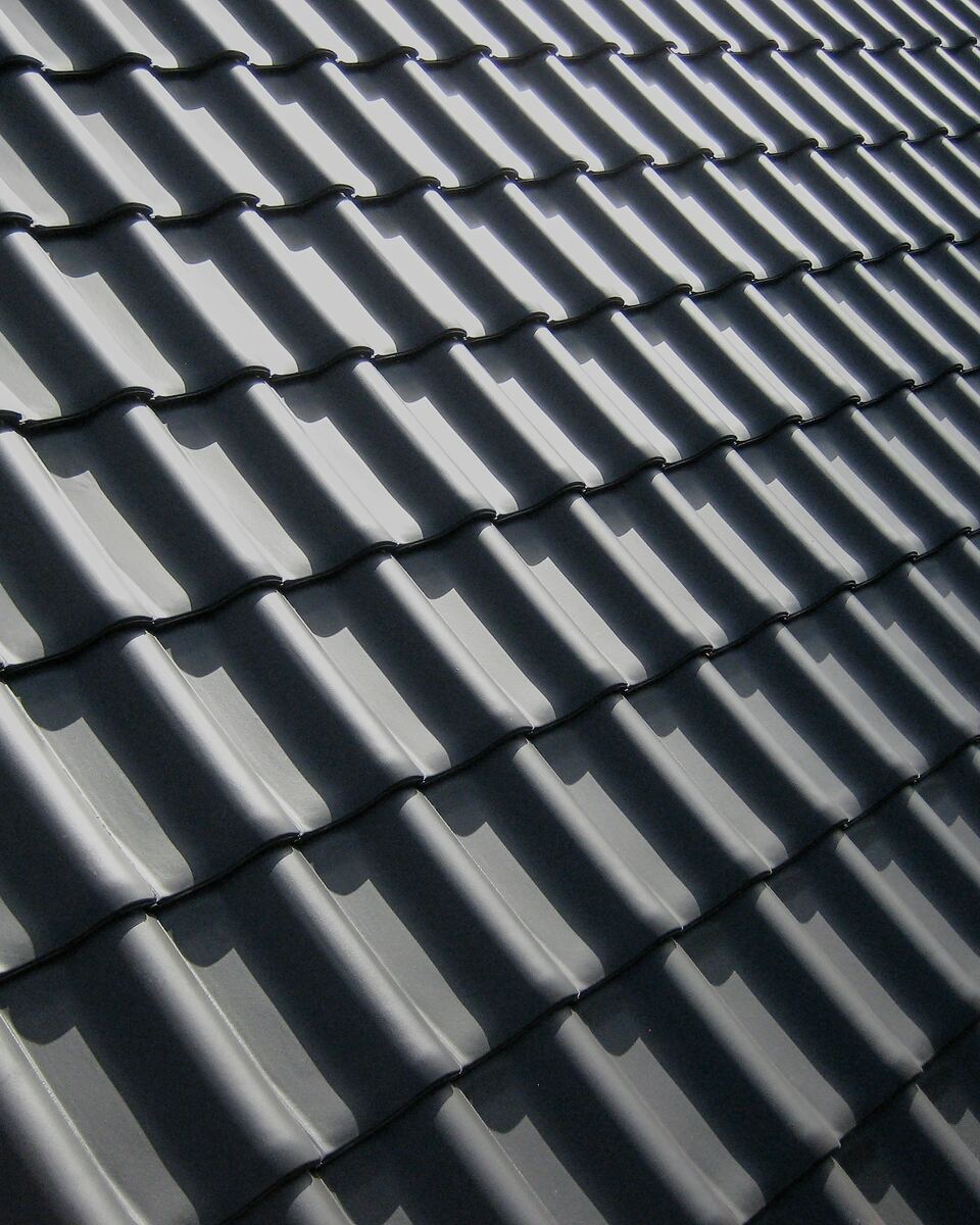 Toiture en tuiles gris anthracite : rangées régulières vues en enfilade, sous une lumière rasante.